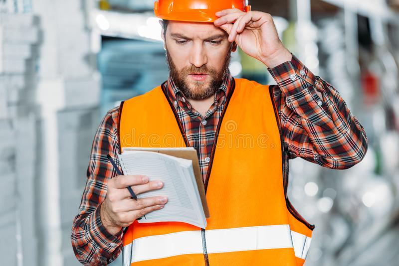 lavoratore-pensieroso-maglia-di-sicurezza-che-considera-blocco-note-deposito-129231262